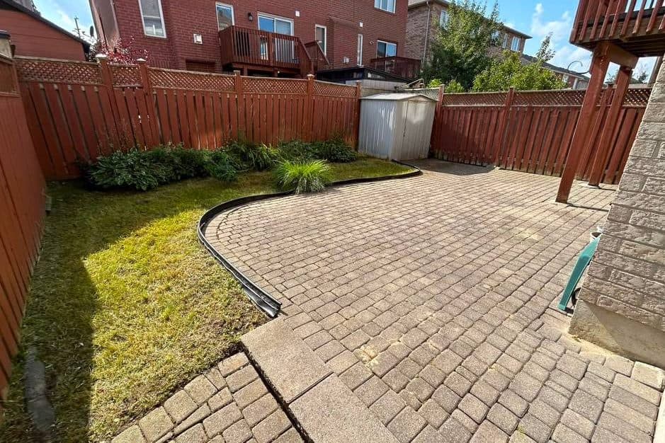 The same patio after work, the paving clear, the lawn cut back and a planted border running along the fence.