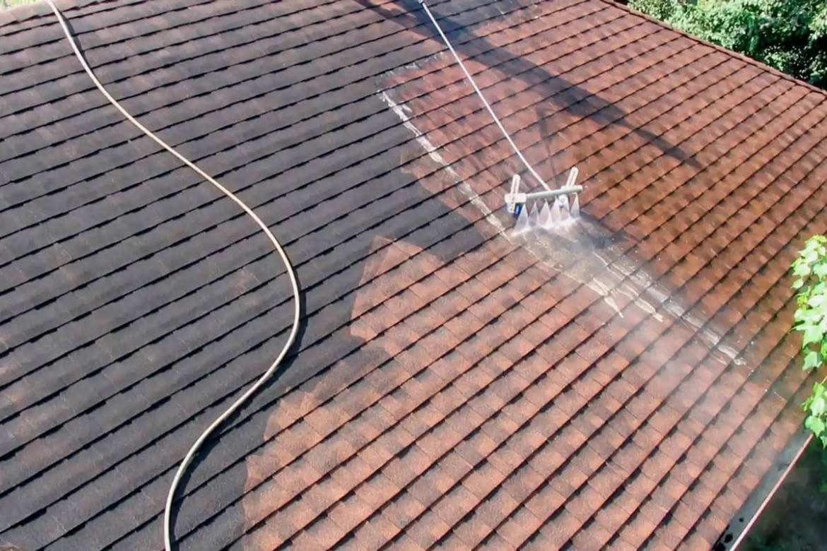 A roof being cleaned with a rotary pressure washer head, a cleaned strip of tile visible behind it and the hose running across the slope.